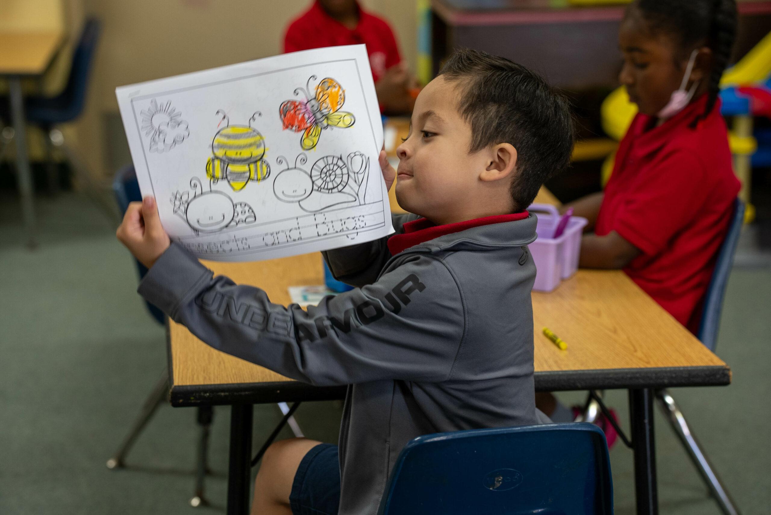 Young student proudly showing his artwork in the early childhood classroom, Orlando Junior Academy